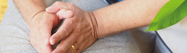 Justierung in der Chiropraktik Manufaktur Kaufmann Zusammengefaltete Hände auf einem grauen Untergrund. An der Hand ist ein Ehering.