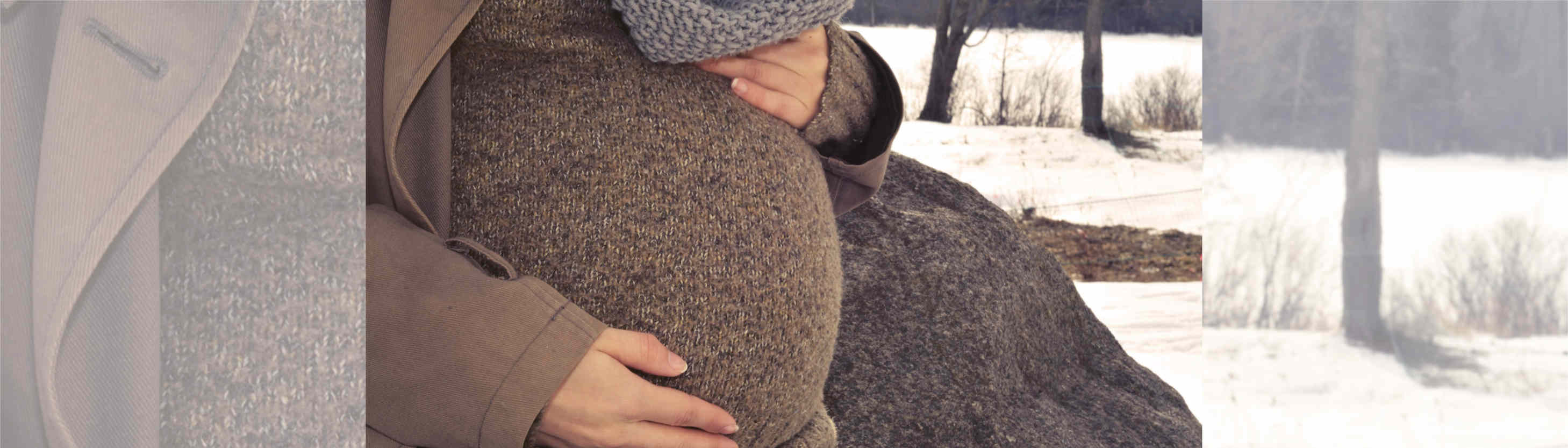 Nahaufnahme eines Schwangerschaftsbauches. Die Frau trägt einen braunen Pullover und einen braunen Mantel.