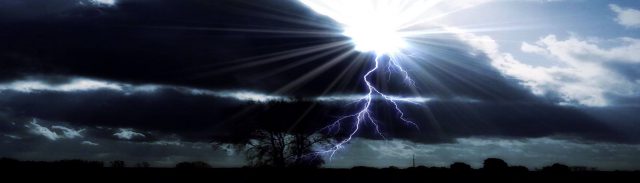 Chiropraktik bei Wetterfühligkeit Ein heller Blitz schlägt in einem Baum ein. Der Himmel ist mit dunklen Wolken bedeckt und die Sonne scheint durch.