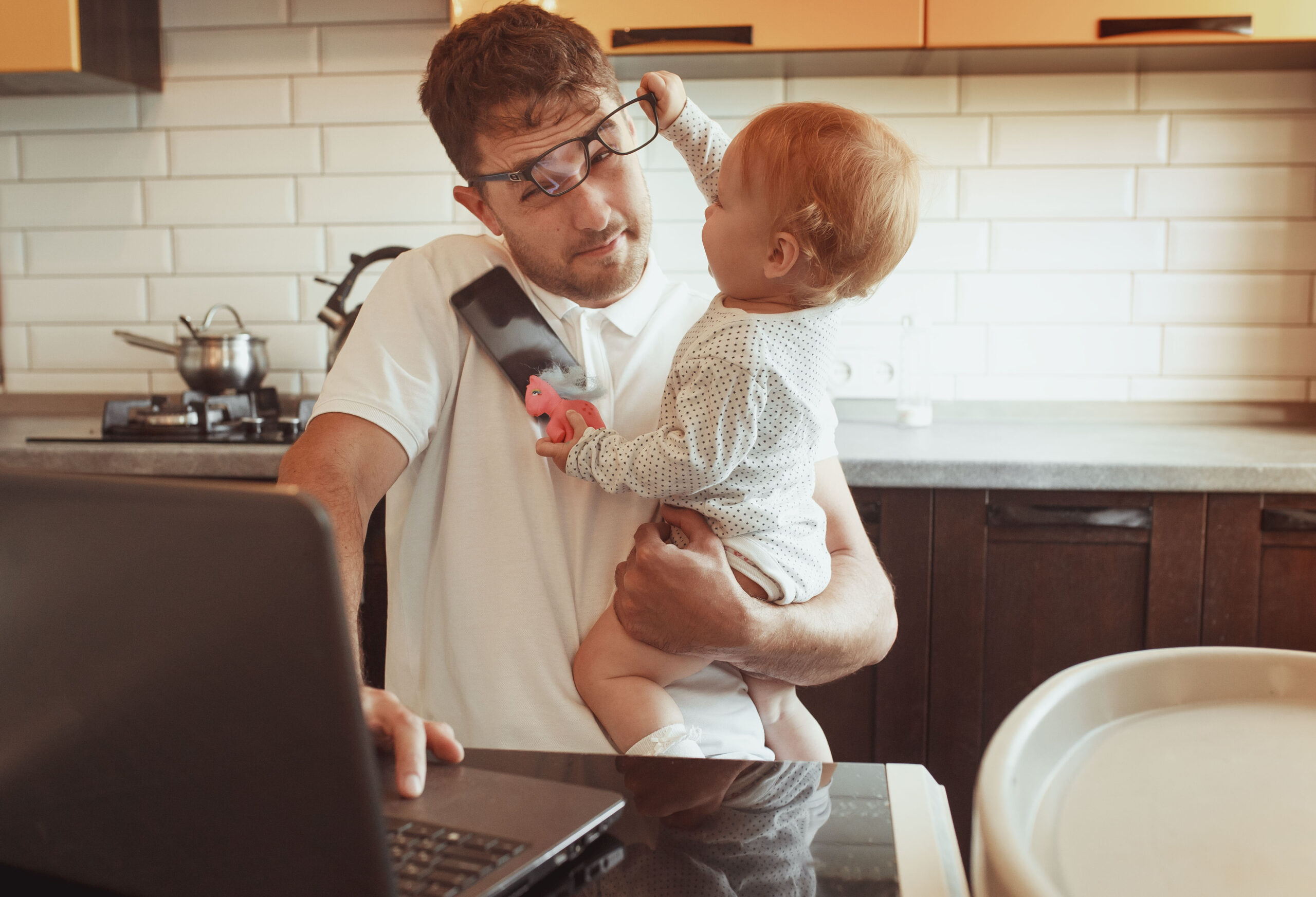 Vater mit dem Baby im Arm in Homeoffice versucht zu arbeiten.