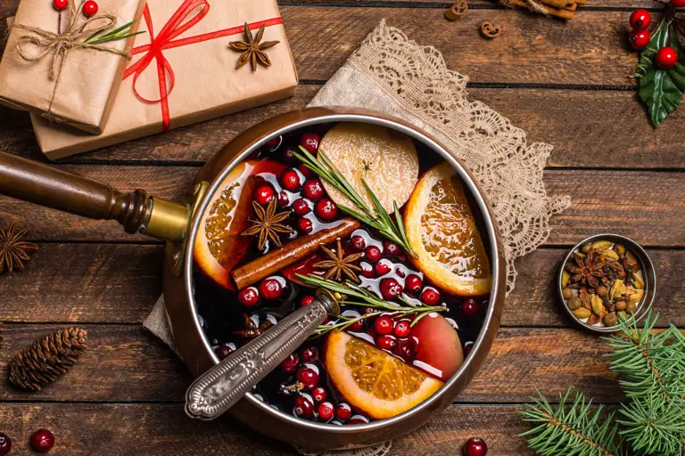 eine Schale Suppe mit Cranberrys und Orangen steht auf einem Holztisch, auf dem auch in braunes Packpapier gewickelte Geschenke liegen