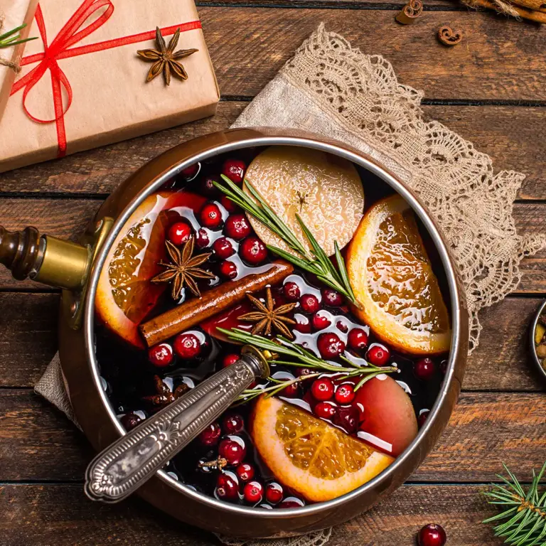 eine Schale Suppe mit Cranberrys und Orangen steht auf einem Holztisch, auf dem auch in braunes Packpapier gewickelte Geschenke liegen