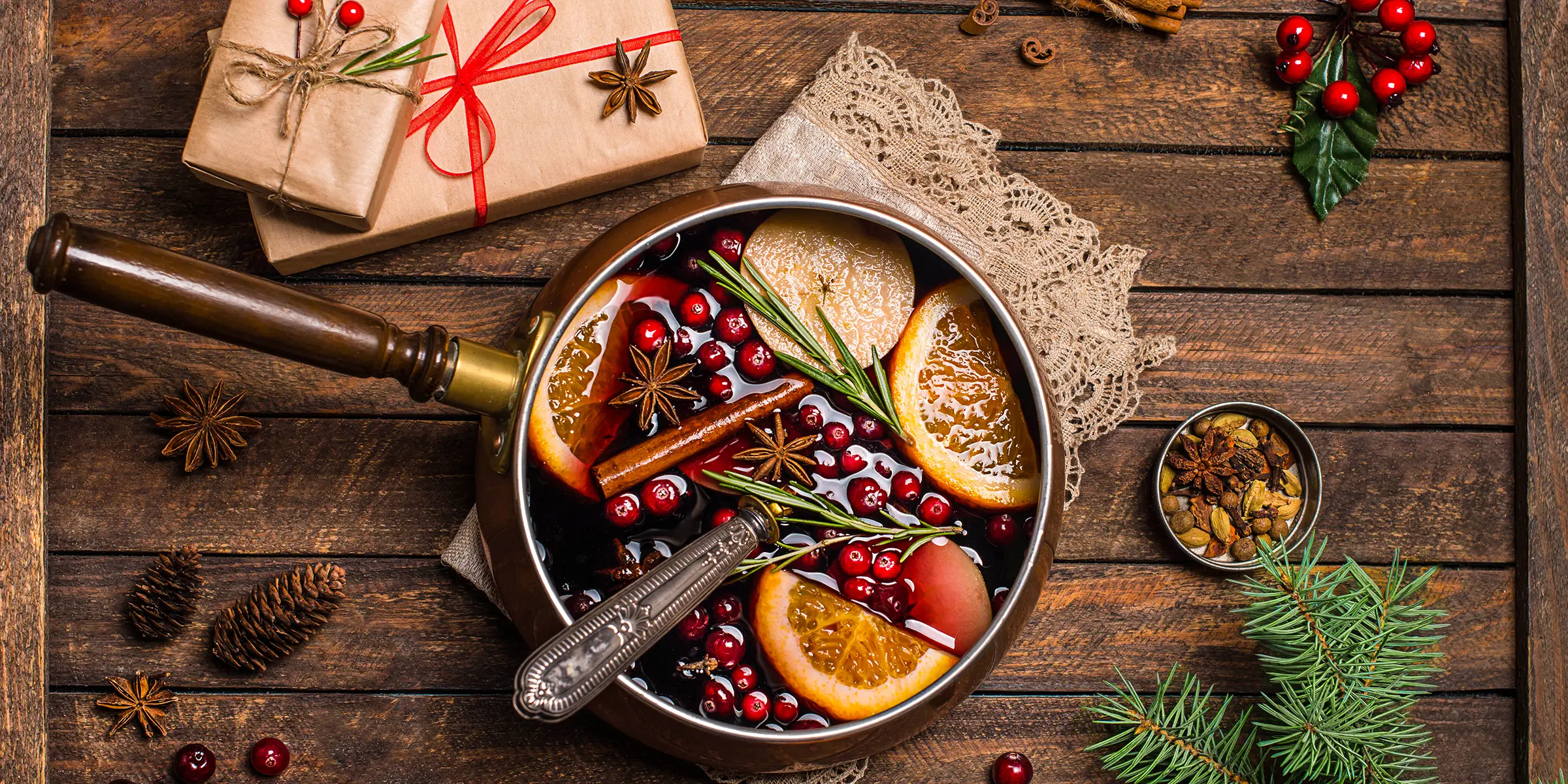 eine Schale Suppe mit Cranberrys und Orangen steht auf einem Holztisch, auf dem auch in braunes Packpapier gewickelte Geschenke liegen