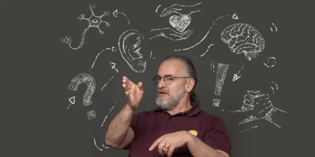 Ein Mann der mit seinen Händen gestikuliert und um den Kreidemotive schwirren