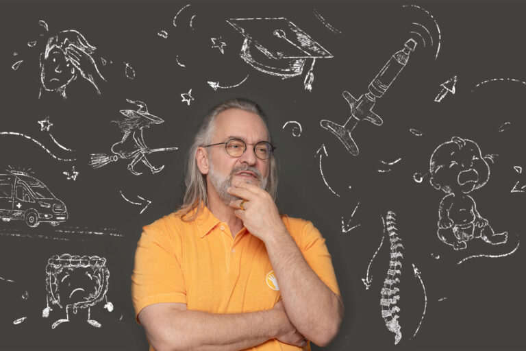 Ein Bild von Ralph Kaufmann der sich nachdenklich ins Gesicht fasst, während er vor einer Kreidemotiv Wand sitzt