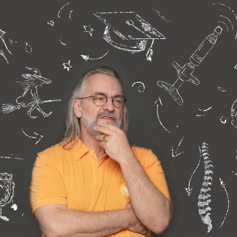 Ein Bild von Ralph Kaufmann der sich nachdenklich ins Gesicht fasst, während er vor einer Kreidemotiv Wand sitzt