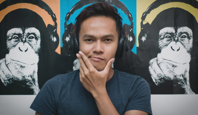 Podcast_2_2400x1400 Ein Mann mit Headset und im Hintergrund hängt ein Bild mit kopfhörertragenden Affen.