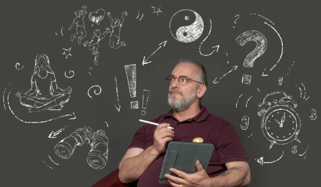 Ein Mann, der ein Tablet und einen elektronischen Stift in der Hand hält, sitzt vor einem grauen Hintergrund mit Kreidemotiven.