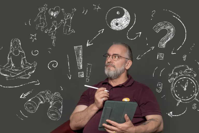 Ein Mann, der ein Tablet und einen elektronischen Stift in der Hand hält, sitzt vor einem grauen Hintergrund mit Kreidemotiven.