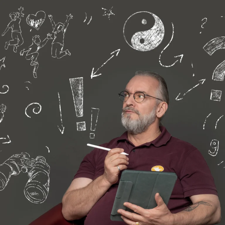 Ein Mann, der ein Tablet und einen elektronischen Stift in der Hand hält, sitzt vor einem grauen Hintergrund mit Kreidemotiven.