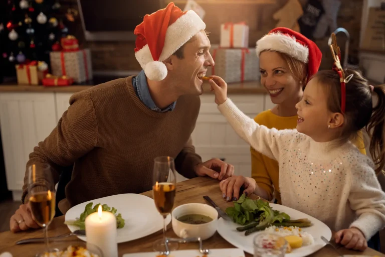 Eine Familie am Weihnachtstisch, bei dem das Mädchen den Vater füttert