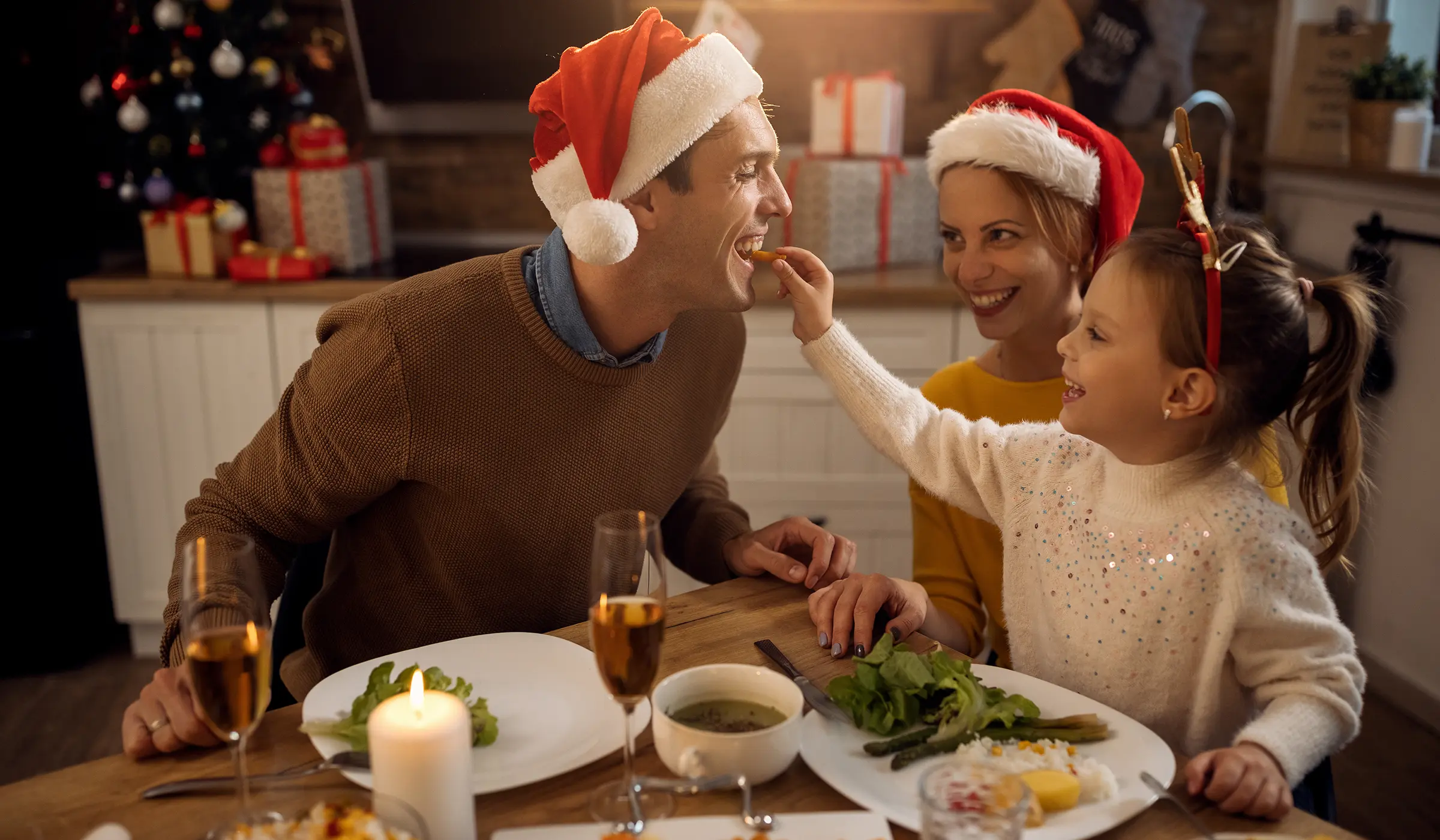 Eine Familie am Weihnachtstisch, bei dem das Mädchen den Vater füttert