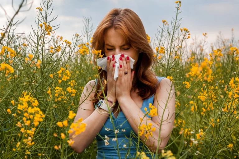 Eine junge Frau steht in einem Blumenfeld und putzt sich die Nase.