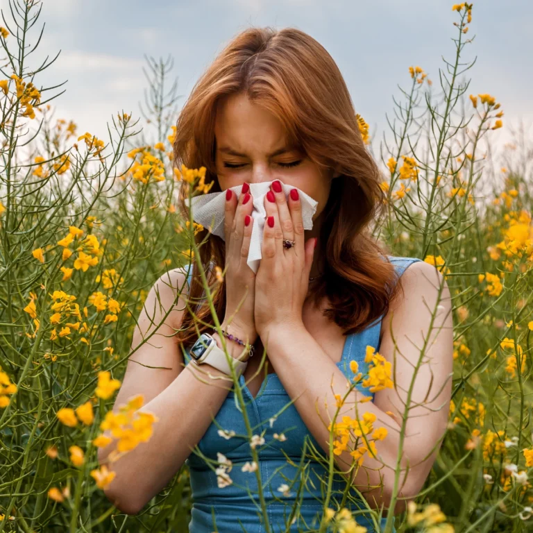 Eine junge Frau steht in einem Blumenfeld und putzt sich die Nase.