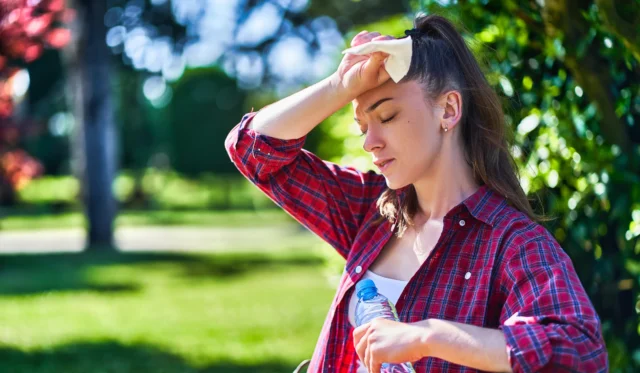 Eine junge Frau wischt sich Schweiss von der Stirn und hält eine Wasserflasche in der Hand.