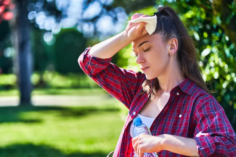 Eine junge Frau wischt sich Schweiss von der Stirn und hält eine Wasserflasche in der Hand.