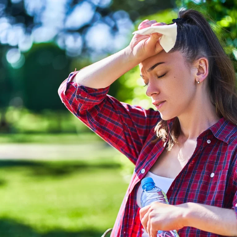Eine junge Frau wischt sich Schweiss von der Stirn und hält eine Wasserflasche in der Hand.